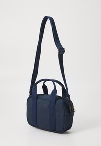 Sac à main bleu marine en tissu robuste, doté de deux poignées supérieures, d'une sangle réglable et de détails de couture sur les sangles.