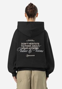 Svart oversized hoodie med ett stort tryck på baksidan. Har text i vitt och silver, samt varumärket "Pegador" längst ner.