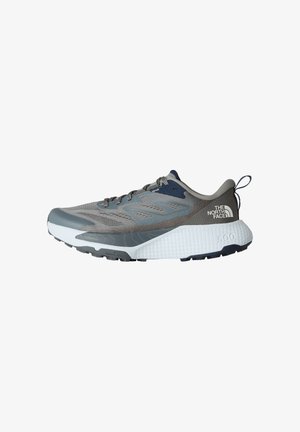 Scarpa sportiva grigia con tomaia in rete, accenti blu navy, suola intermedia bianca texturizzata e suola in gomma nera. Presenta lacci e un'etichetta sul tallone.