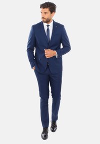 Completo blu navy realizzato in tessuto morbido, vestibilità su misura, giacca monopetto, cravatta coordinata e scarpe nere lucide. Dettagliato con un fazzoletto da taschino.