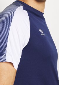 Námořnická a bílá sportovní tričko s úzkým střihem. Obsahuje diagonální pruhovaný vzor na rameni. Vyrobeno z prodyšného syntetického materiálu.