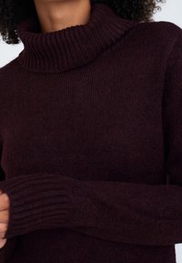 Burgundy polokrage tröja i strukturerad stickad tyg, med ribbade manschetter. Designen ger en avslappnad passform och varm täckning.