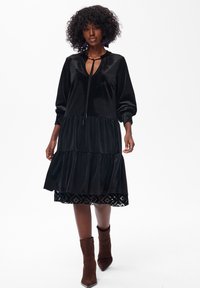 Czarna aksamitna sukienka o warstwowym designie, z długimi rękawami i dekoltem w kształcie łezki. Wykończona koronką na dołach oraz fakturowanymi rękawami.