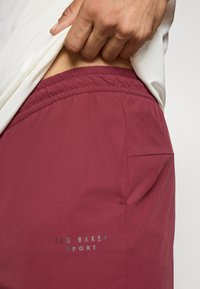 Bordo sporta šorti ar elastīgu jostu, maigu tekstūru un sānu kabatu. Ar sudrabā drukātu "TED BAKER SPORT".