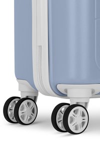 Harde koffer in lichtblauw met een gestructureerde afwerking, witte rits en vier multidirectionele spinnerwielen met zwarte rubberen accenten.