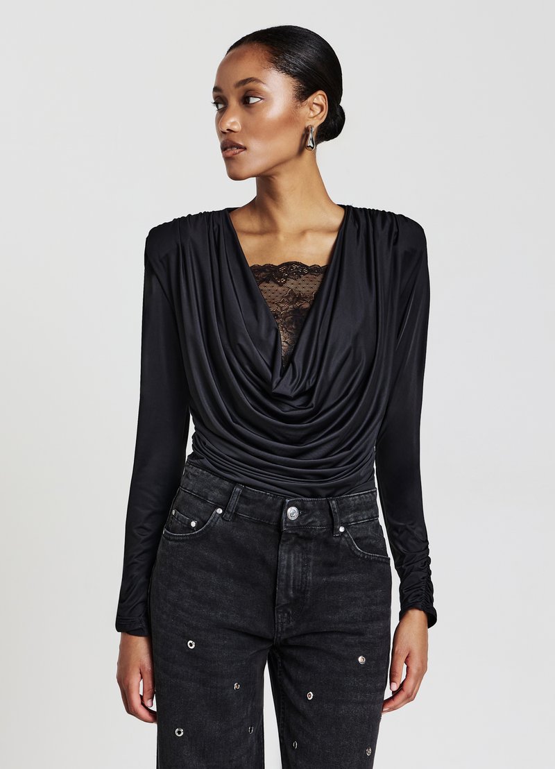 Schwarzes, drapiertes Oberteil mit langen Ärmeln und Spitze am Ausschnitt, kombiniert mit hoch taillierten schwarzen Jeans mit metallischen Akzenten.