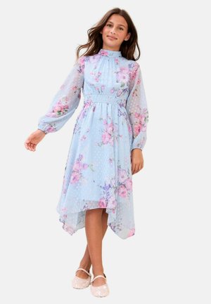 Mergina, dėvinti šviesiai mėlyną, ilgomis rankovėmis, gėlių raštais puoštą midi suknelę su aukštu kaklu ir permatomomis rankovėmis, derančią su žėrinčiomis baltomis Mary Jane tipo bateliais.