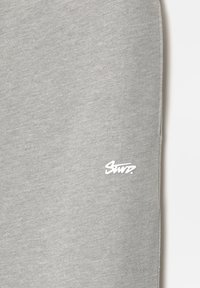 Grijze sweatshirtstof met een zachte textuur, voorzien van een prominent wit logo op de voorkant. Eenvoudig ontwerp zonder patronen of accenten.