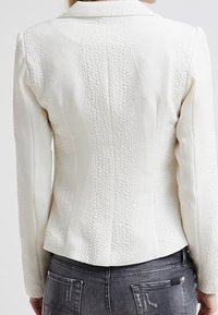 Blazer blanc texturé à manches longues, silhouette ajustée, col cranté et motif géométrique subtil sur la surface. Vue de dos.