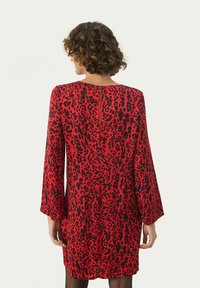 Rød leopardprint kjole med lange klokkeærmer, en rund halsudskæring og en nøglehulsgabning i ryggen. Glat stof med en afslappet pasform.