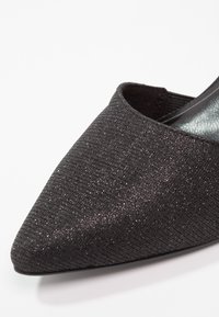 Chaussure en tissu noir avec un bout pointu, surface texturée offrant un léger brillant et un design à dos ouvert pour un enfilage facile.