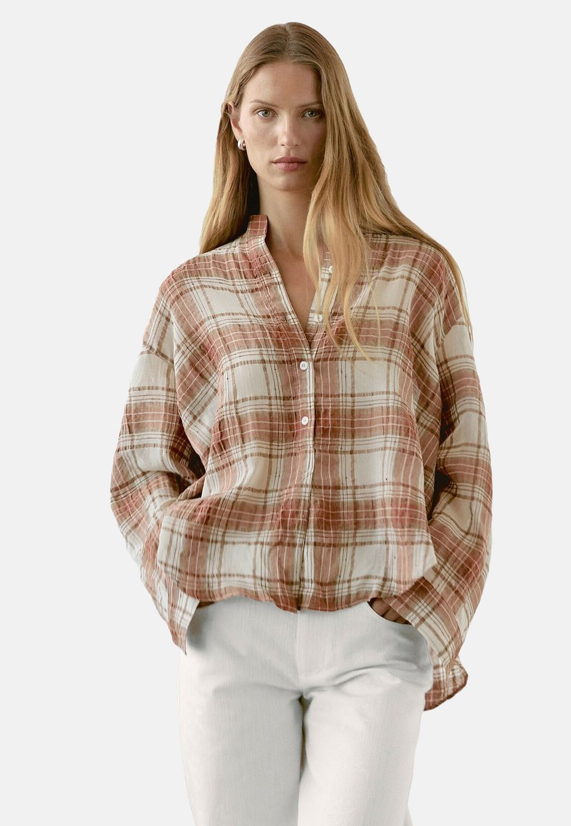 Langärmliges, knöpfbares Hemd in einem karierter Muster aus Beige, Rot und Orange, mit entspannter Passform und Kragen. Getragen mit weißen Hosen.