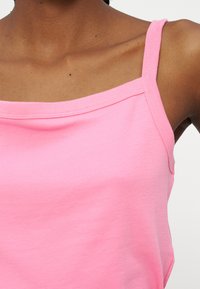 Κοντινό πλάνο ενός ατόμου που φοράει ένα ροζ αμάνικο τοπ, με ορατούς τους ώμους, την κλείδα και το πάνω μέρος του στήθους, όπου φαίνονται μικρές ελιές.