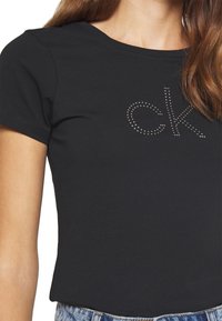 Czarny bawełniany t-shirt z krótkim rękawem z błyszczącym logo "ck" wykonaną z małych kryształków z przodu. Klasyczny krój i okrągły dekolt.
