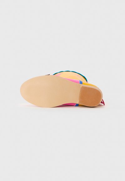 Flat light brown sole of a colorful boot with yellow, pink, and blue accents, shown from the bottom on a white background.