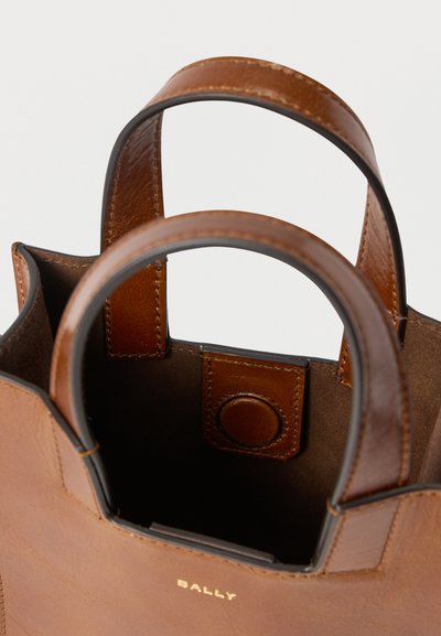 Καφέ δερμάτινη τσάντα με ομαλή υφή και δομημένο σχέδιο. Διαθέτει στρογγυλεμένες λαβές και κυκλικό κούμπωμα με κουμπί. Ο χρυσός λογότυπος "BALLY" είναι ορατός.