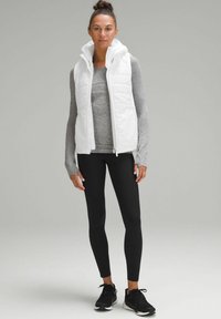 Gilet bianco puffoso con cappuccio sopra un top grigio a maniche lunghe, abbinato a leggings neri e scarpe da ginnastica nere. Tessuto liscio e leggero.