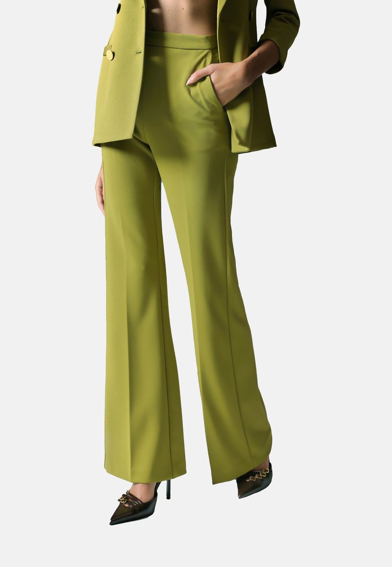 Donna che indossa pantaloni a palazzo su misura verde lime e un blazer abbinato, con tacchi a punta neri, mano nella tasca, tagliato all'altezza del torso.
