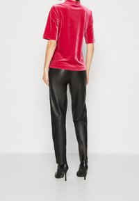 Haut en velours rose à manches courtes associé à un pantalon en cuir noir et des bottes noires à talons hauts, mettant en avant des textures lisses et un design épuré.