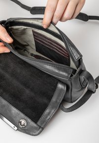 Zwarte leren en suède handtas met een gestreepte binnenkant, voorzien van een ritsvak, kaartsleuven en rode stiksel-details.