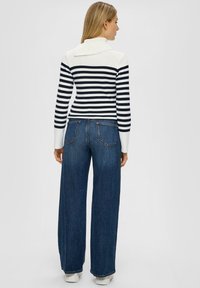 Gestreifter Strickpullover in Weiß und Marineblau mit umgeschlagenem Kragen, kombiniert mit weit geschnittenen, dunklen Jeans aus Denim mit Gesäßtaschen und sauberen Säumen.