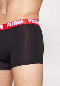 Schwarze Boxershorts mit einem roten Gummibund, auf dem "PUMA" in weißen Buchstaben steht. Der Stoff sieht glatt und eng anliegend aus.
