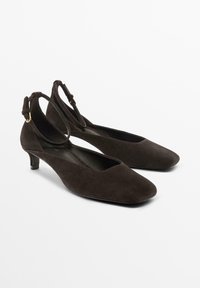 Brown suede slingback shoes with a square toe and a small heel. Features an adjustable strap with gold-tone hardware.