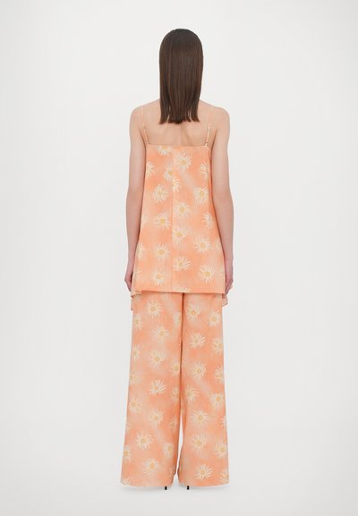 Twee-delig outfit in een lichte oranje kleur, bestaande uit een mouwloze top en wijde broek, beide versierd met een bloemenpatroon.