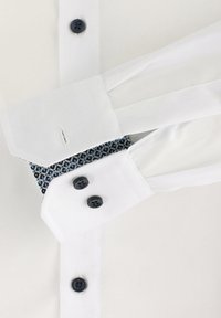 Weißes Hemd mit französischen Manschetten, ausgestattet mit dunkelblauen Knöpfen und einem gemusterten blauen und weißen Manschettenfutter. Sanfte Textur und maßgeschneiderter Schnitt.
