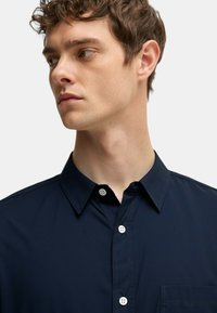 Camicia blu navy con bottoni e colletto, dotata di taschino sul petto e bottoni bianchi. Tessuto morbido e dettagli di cucitura puliti.