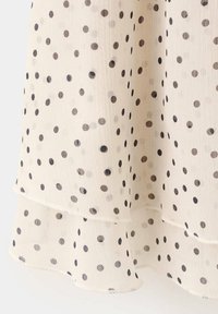 Tissu crème transparent avec ourlet à plusieurs couches présentant des pois noirs et gris de tailles variées.