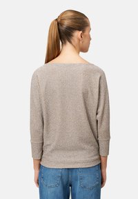Hellbeiger Pullover mit strukturiertem Muster, ¾-Ärmeln und weitem Ausschnitt, kombiniert mit blauen Jeans.