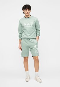 Lysegrønt loungewear sæt i bomuld med en langærmet trøje og shorts med logo-tryk. Trøjen har rund hals; shorts har elastisk taljebånd.