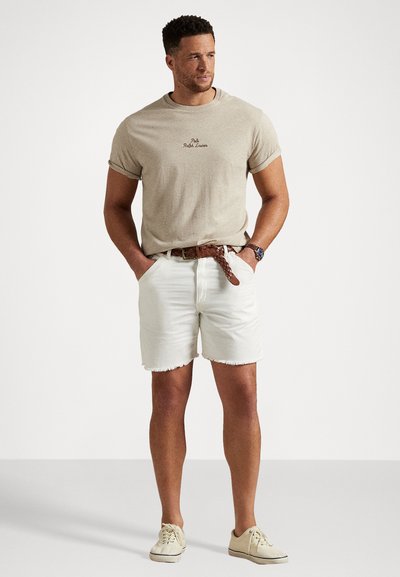 Beige kokvilnas t-krekls ar izšūtu logo, balti džinsu šorti ar saplēstu malu, brūns pītā josta un gaismas krāsas ikdienas apavi.