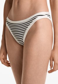 Kvinna iklädd svart och vit randig bikiniunderdel med vit kant, som visar mellansektion och övre lår mot vit bakgrund.