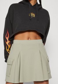 Zkrácená černá mikina s grafickými vzory ohně na rukávech; zkombinována s bledě zelenou sukní šortkami s sklady a bočními cargo kapsami.