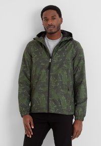 Green patterned jacket with a hood, featuring a front zipper, elastic cuffs, and a lightweight, textured fabric. Worn over a gray shirt.