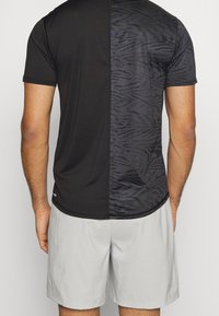 Camiseta deportiva negra con un lado liso y un lado con estampado de animal negro texturizado, con dobladillo redondeado y mangas cortas.