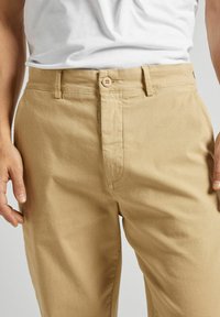 Chinos caqui de algodón, con cierre de cremallera, un botón de cierre y bolsas estándar. Textura suave con un ajuste entallado.