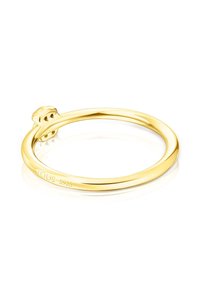 Prosty, polerowany złoty pierścionek z małym detalem w kształcie misia na obrączce oraz wygrawerowanym napisem "TOUS S925" wewnątrz.