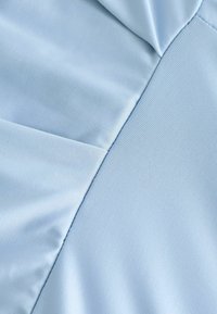 Jasnoniebieska tkanina o gładkiej fakturze, z detalami szwu i subtelnymi zmarszczkami, wskazującymi na zwisający krój.