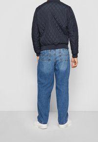 Marinblå quiltad bomberjacka med ribbade muddar, parat med ljusblå löst sittande denimjeans. Vita sneakers fulländar outfiten.