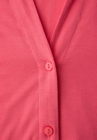 Cardigan rose corail avec un col en V, une texture côtelée douce et de petites boutons assortis le long du devant pour la fermeture.