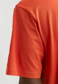 Kurzärmliges T-Shirt in leuchtendem Orange, aus weichem Baumwollstoff gefertigt. Glatte Textur mit rundem Ausschnitt und sauber genähtem Saum und Ärmeln.