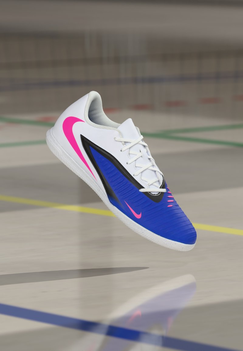 Αθλητικό παπούτσι Nike με μπλε επάνω μέρος με υφή, λευκές λεπτομέρειες, ροζ λογότυπο και μαύρες λεπτομέρειες, σχεδιασμένο για εσωτερική χρήση.