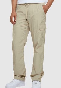Beige cargobroeken met een elastische tailleband en koord. Voorzien van zijzakken en een losse pasvorm. Gecombineerd met witte sneakers.