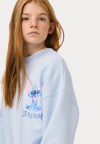 Felpa blu chiaro con collo a coste, caratterizzata da una grafica vibrante di Stitch e dalla scritta "Stitch" in grigio chiaro sul davanti.
