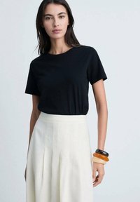 Tricou negru cu mâneci scurte, asortat cu o fustă plisată crem, cu talie înaltă. Brățări din plastic transparent în culorile negru, portocaliu și bej.