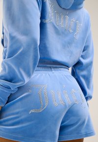 Blue velour loungewear set featuring "Juicy" embellished with rhinestones on the hoodie and shorts, showcasing a soft texture and relaxed fit.
