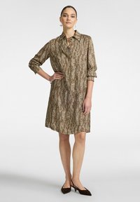 Vestido camisas de estampado de leopardo marrón con cuello, mangas enrolladas y corte holgado. La tela texturizada añade interés visual. Combinado con zapatos marrones oscuros.
